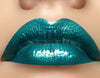 Green Metallic Emerald City Lip Gloss swatch showing turquoise green shade over lipstick for bold makeup lovers.
